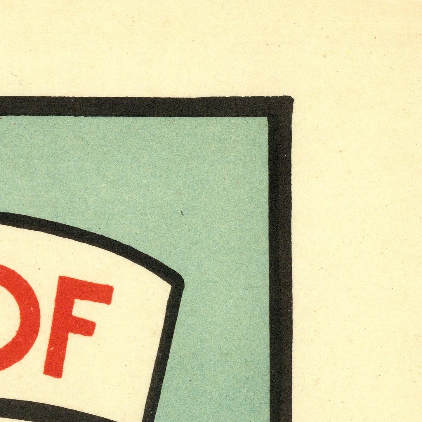 A close-up detail of a graphic print or sign showing a light blue-green square with a thick black border, a white curved label area, and red lettering on a cream background.